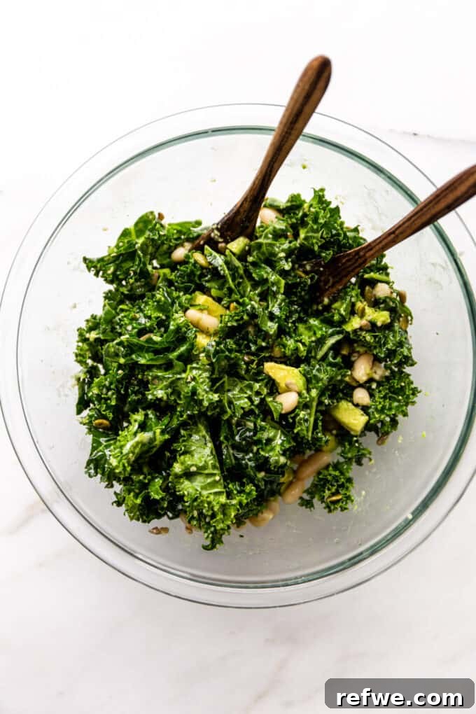 Hearty Kale and White Bean Power Bowl 6 Kale and white bean salad being gently tossed in a clear mixing bowl with wooden serving spoons