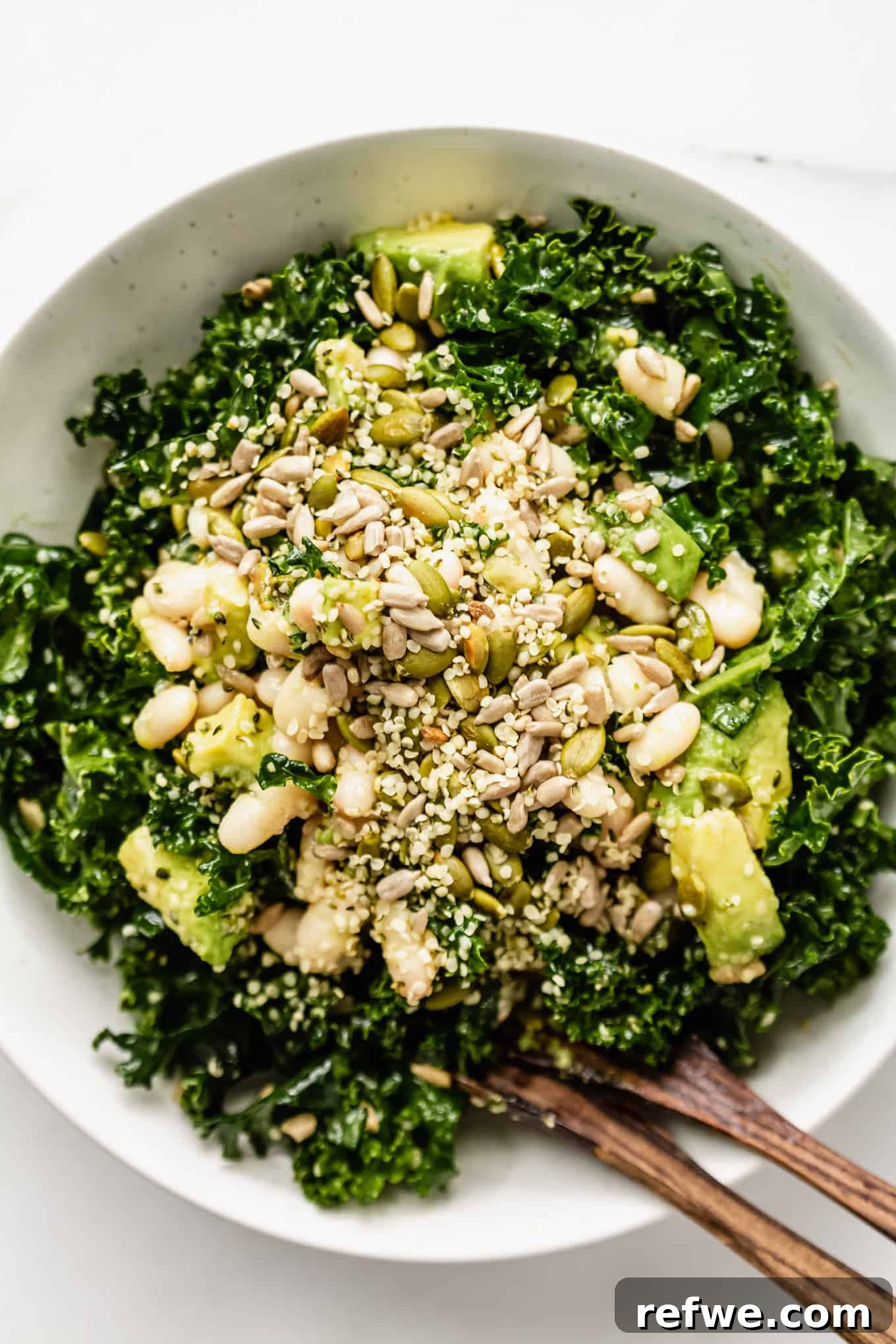 Hearty Kale and White Bean Power Bowl 8 Kale and white bean salad in a bowl with two wooden serving spoons, ready to be enjoyed