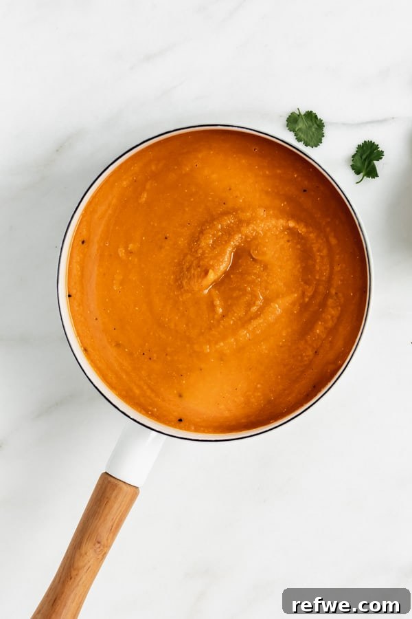 Hearty Spiced Sweet Potato, Lentil, and Carrot Soup 4 A white pot brimming with a rich, orange-hued carrot, lentil, and sweet potato soup, ready to be served and enjoyed.