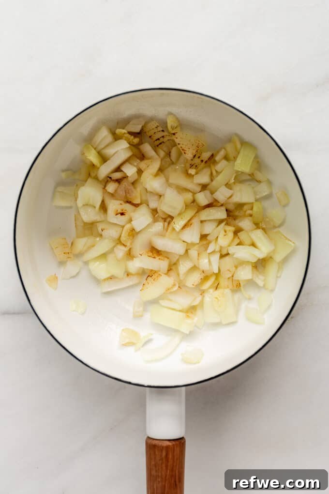 Chopped onions and minced garlic gently sautéing in olive oil in a white pot, releasing their aromatic flavors.
