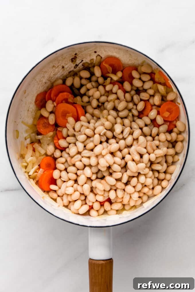 White beans, carrots, and onions mixed in a white pot, ready for the next delicious ingredients.