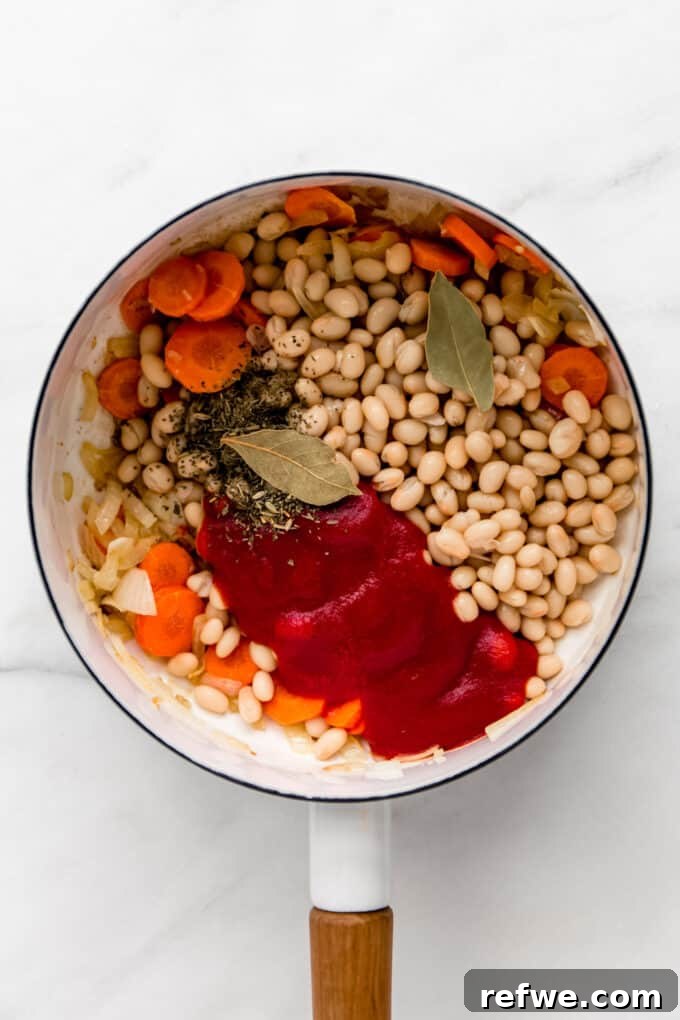 A colorful medley of white beans, vegetables, herbs, and crushed tomatoes expertly combined in a white pot.