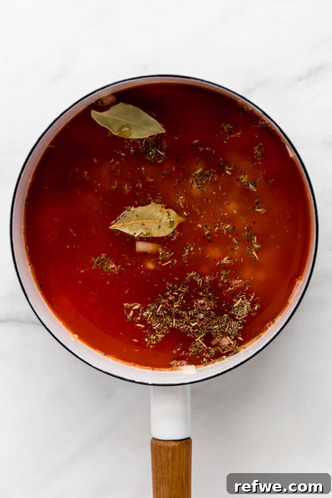 Soup broth simmering in a white pot with herbs, developing rich and aromatic flavors.