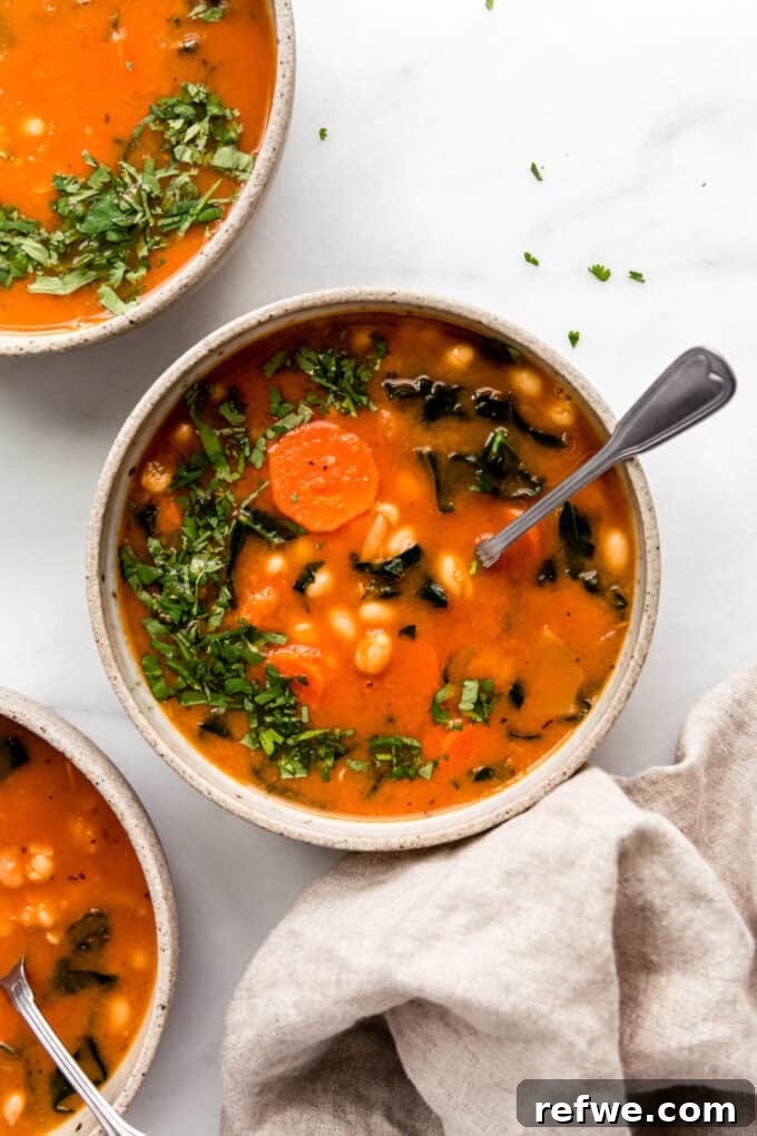 Three beautifully presented bowls of white bean and kale soup, garnished and ready to be served.