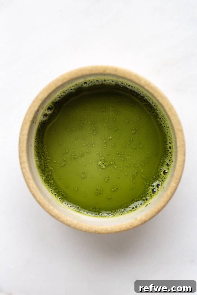 Zen Matcha Chill 4 Matcha powder mixed with warm water in a small ceramic bowl, with a bamboo whisk next to it, indicating the first step of preparation.