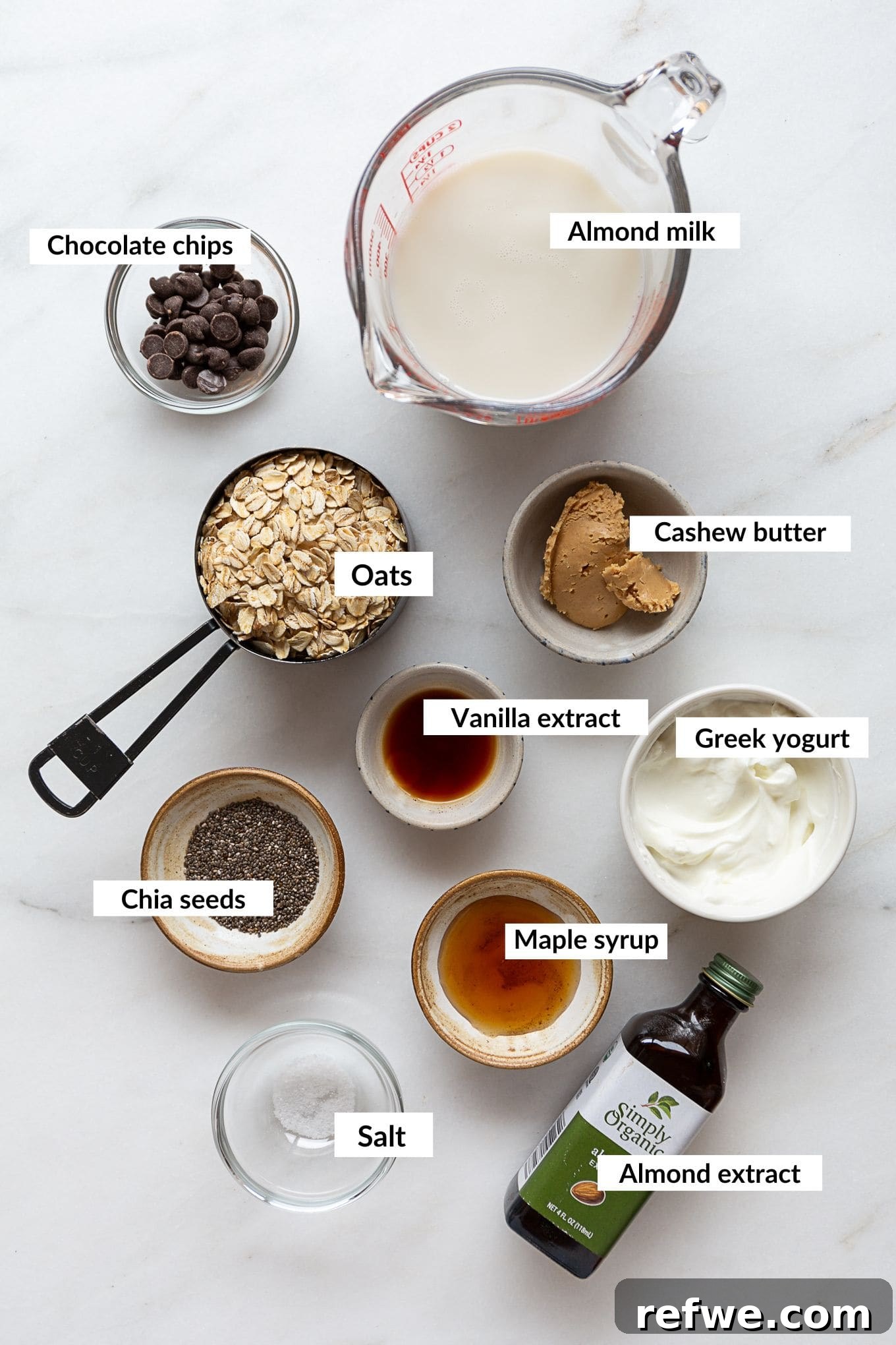 Dreamy Cookie Dough Oats 3 A selection of ingredients laid out, including oats, chia seeds, cashew butter, almond extract, and chocolate chips, ready to make cookie dough overnight oats.