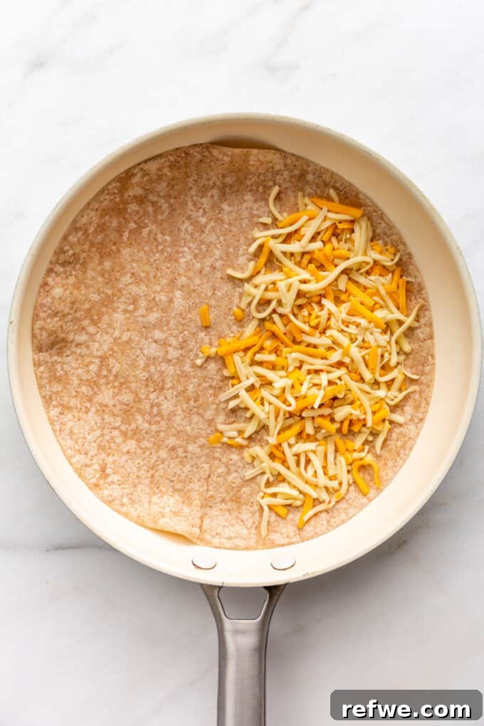 Fiesta Black Bean and Corn Quesadillas 6 Shredded cheese being sprinkled onto half of a large tortilla in a pan.