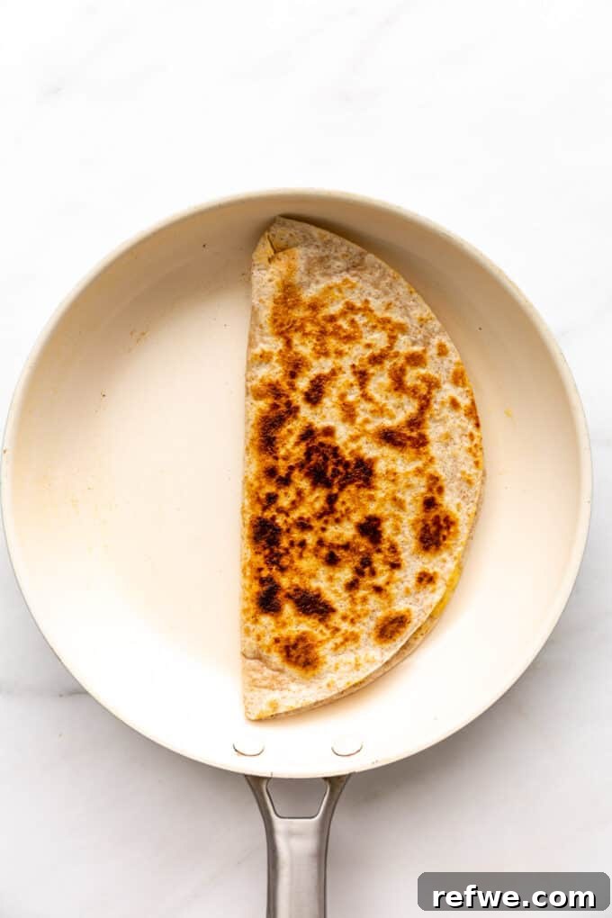Fiesta Black Bean and Corn Quesadillas 9 A crispy black bean and corn quesadilla cooking in a pan with melted cheese oozing slightly.