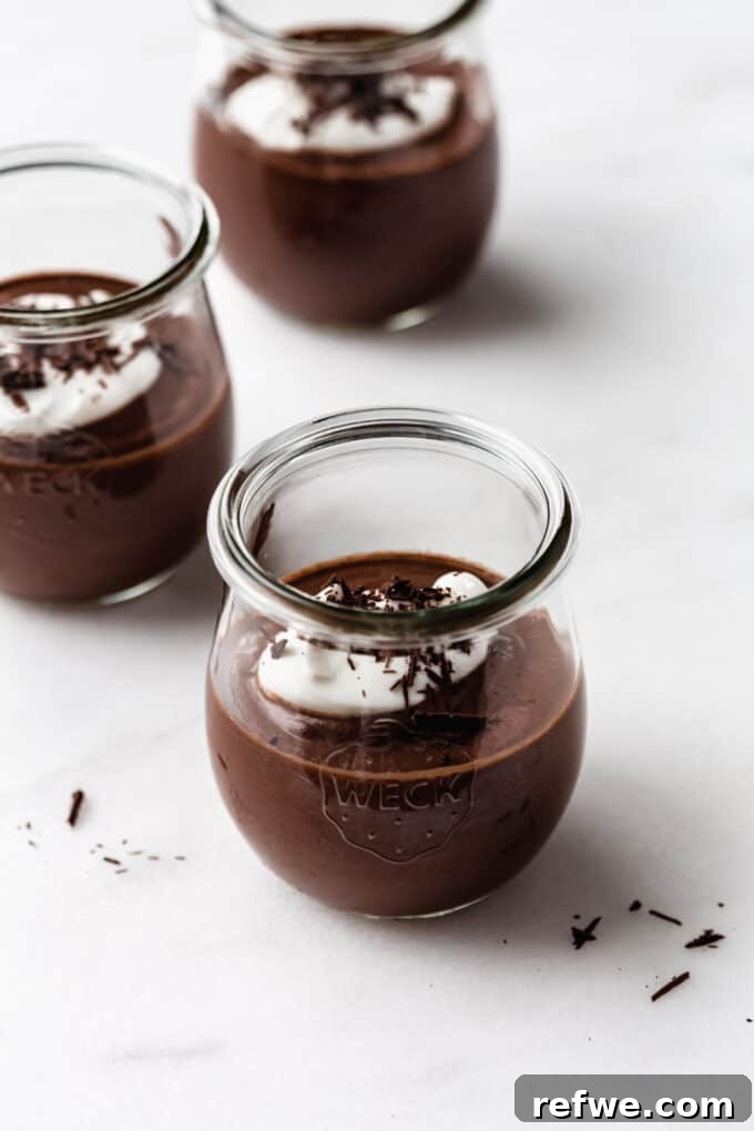 Three cups of decadent vegan chocolate pudding topped with fluffy coconut yogurt and chocolate shavings, presented beautifully for a healthy dessert.