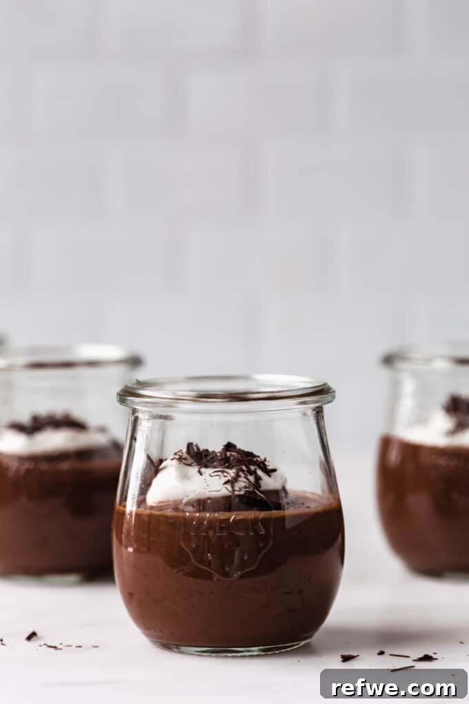 Three beautifully presented cups of vegan chocolate pudding, resting on a sophisticated marble counter, ready to be enjoyed.