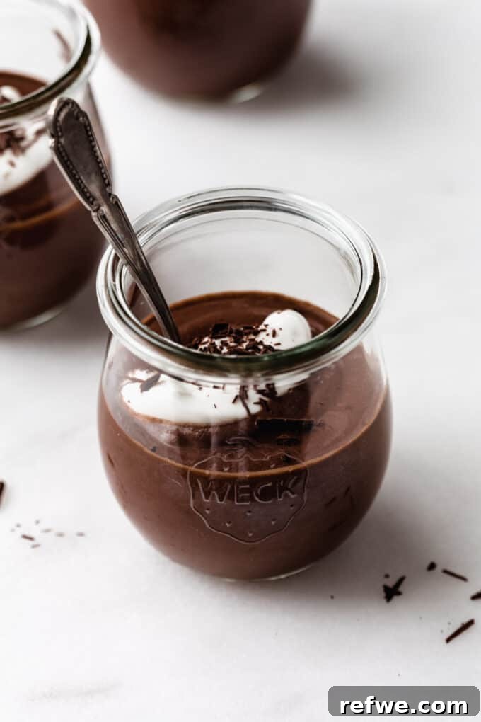 A single serving of smooth, rich vegan chocolate pudding in a clear glass cup, with a spoon ready to dig in, highlighting its creamy texture.