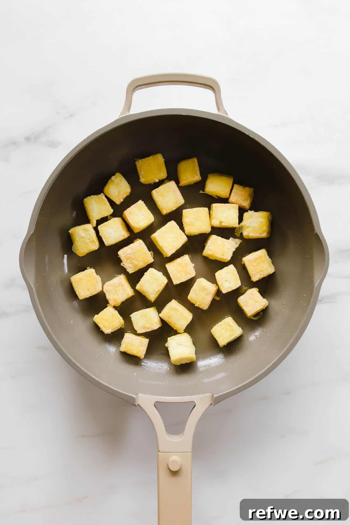 A non-stick pan filled with an array of golden-brown, crispy tofu cubes, sizzling gently as they finish cooking to perfection.