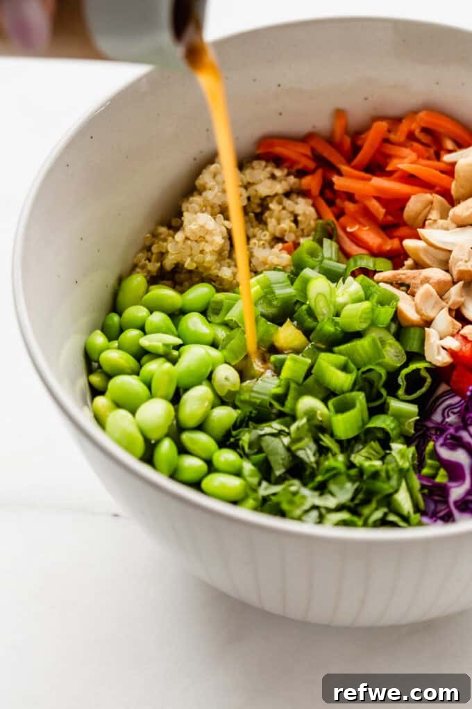 Wholesome Quinoa Edamame Crunch Bowl 5 Edamame salad in a large bowl with sesame dressing being poured into it, highlighting the vibrant dressing