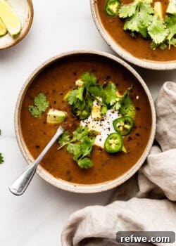 Two enticing bowls of black bean soup, beautifully garnished, resting on a rustic wooden surface with a beige napkin nearby.