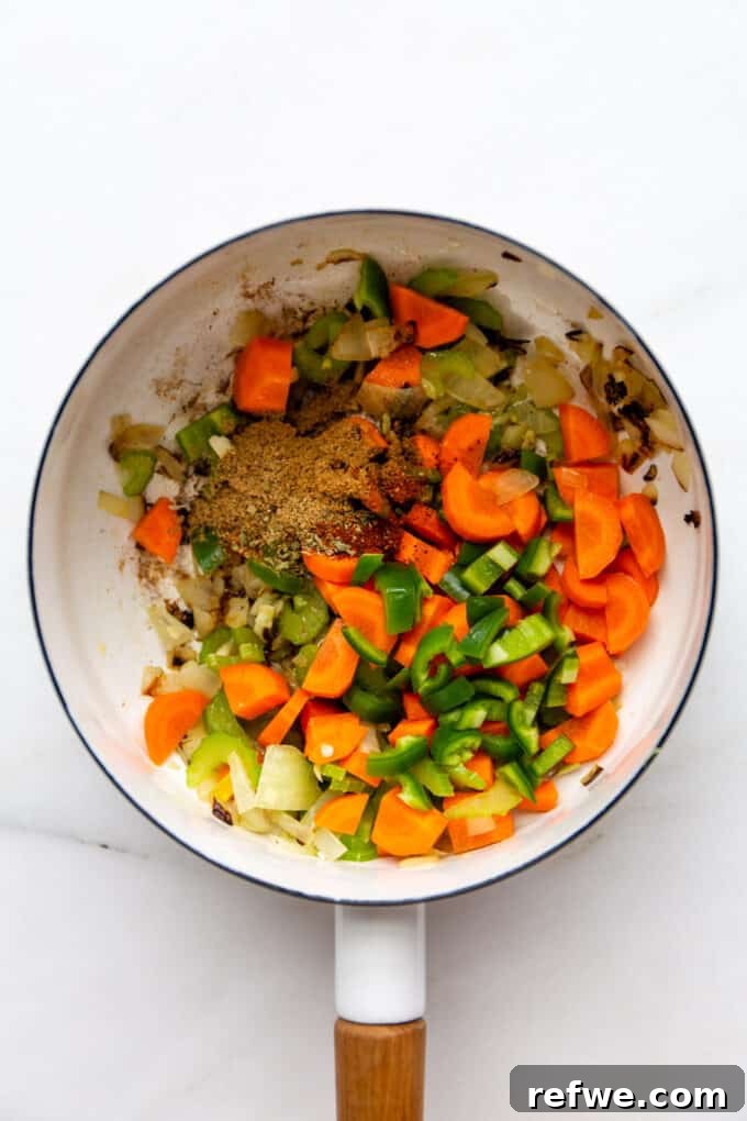 Spices and Vegetables Sautéing Together A mix of chopped vegetables, including carrots and jalapenos, combined with spices in a white pot, actively sautéing to release their flavors.