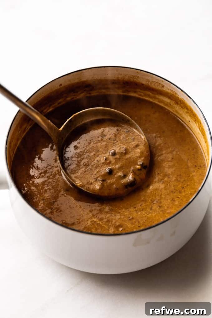 Stirring Black Bean Soup Rich black bean soup being gently stirred with a ladle in a white pot, showcasing its deep color and inviting texture.