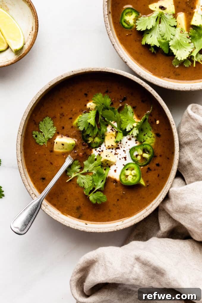 Two Bowls of Vegan Black Bean Soup Two enticing bowls of black bean soup, beautifully garnished, resting on a rustic wooden surface with a beige napkin nearby, ready to be enjoyed.