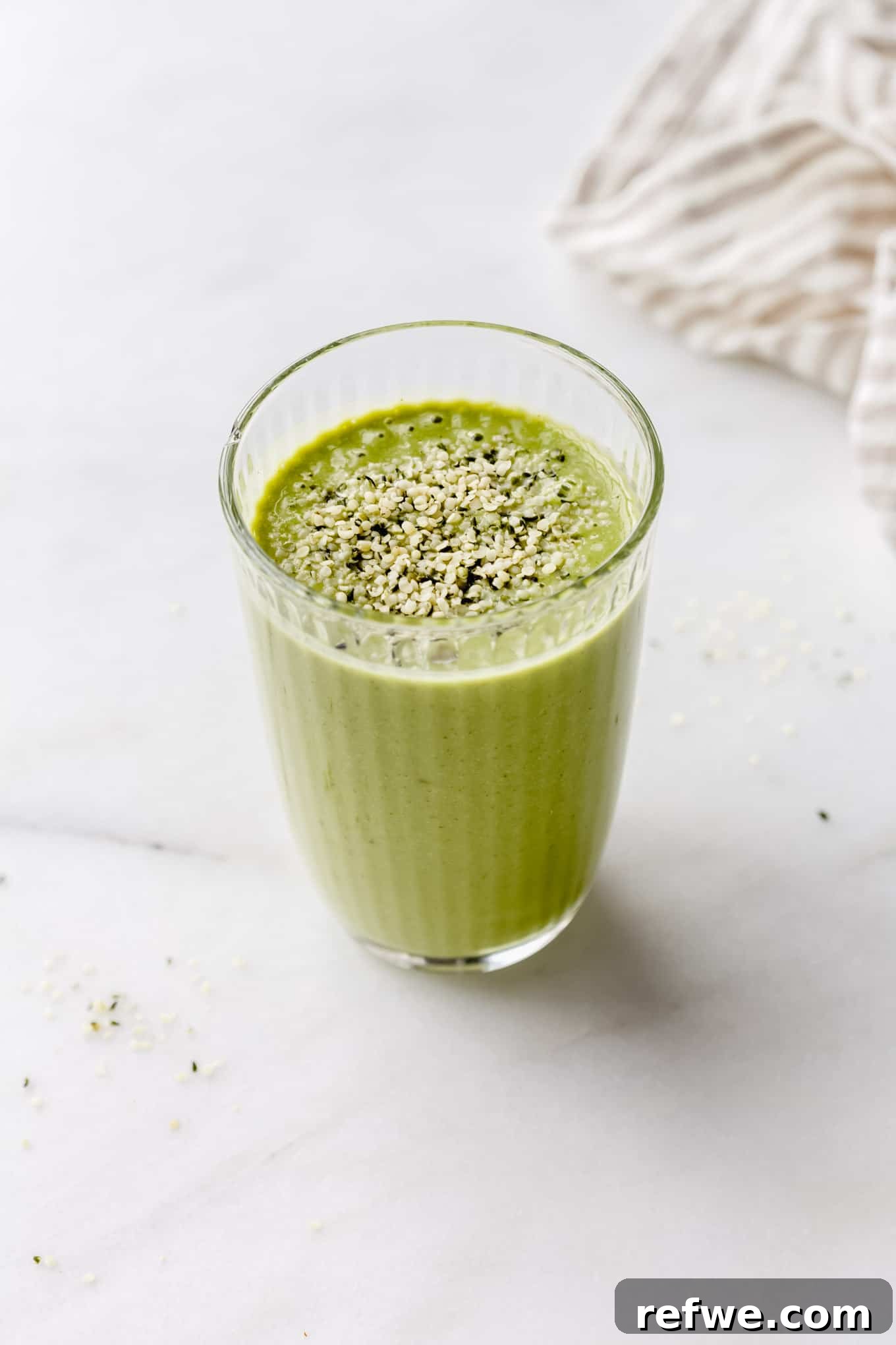Supercharged Green Protein Smoothie 6 A vibrant green protein smoothie, topped with a sprinkle of hemp seeds, is presented in a clear glass, ready to be enjoyed as a refreshing and nutritious drink.