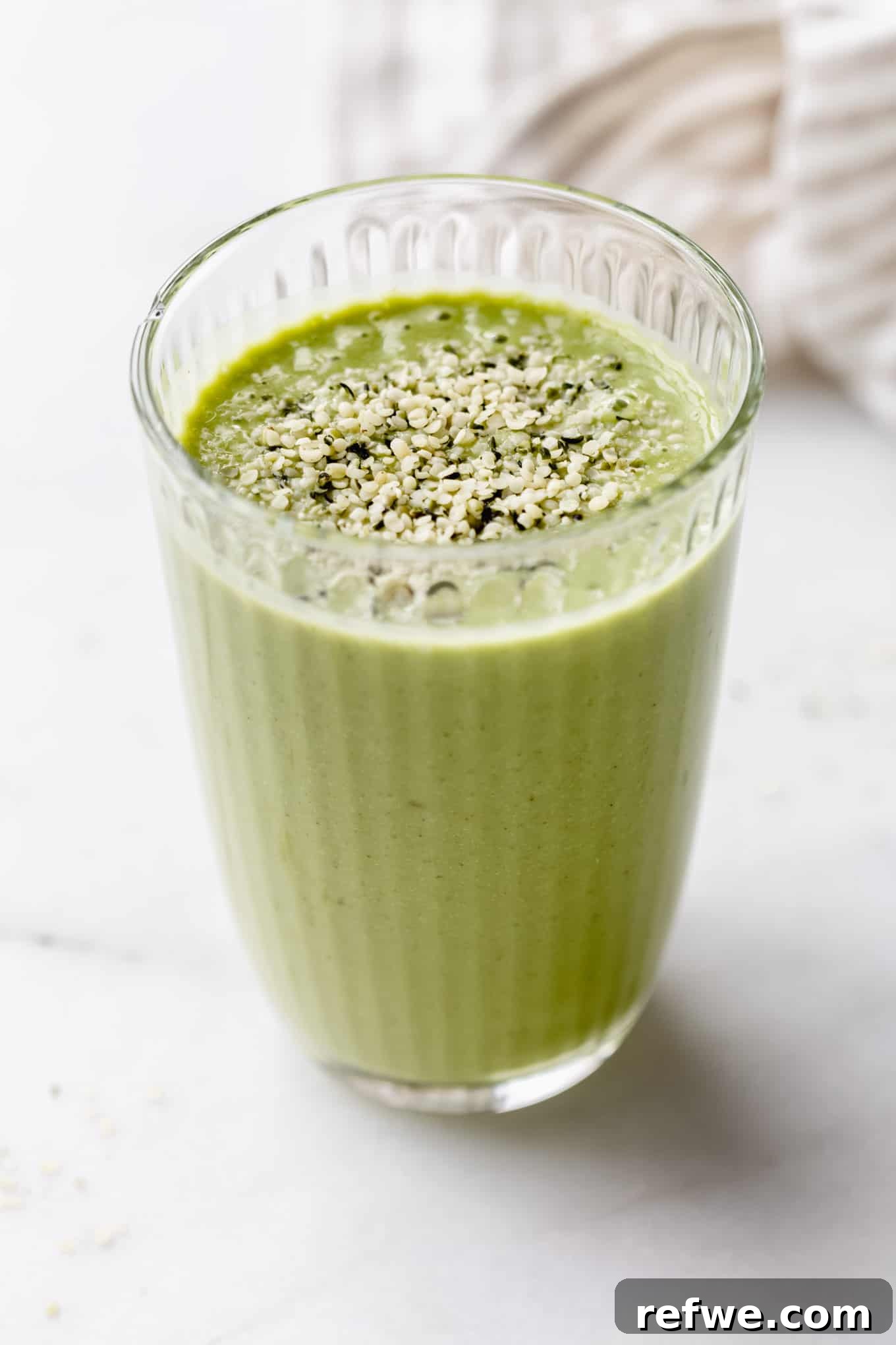 Supercharged Green Protein Smoothie 7 A refreshing green protein smoothie in a glass, topped with a sprinkle of healthy hemp seeds, sits on a rustic wooden surface, embodying natural goodness.