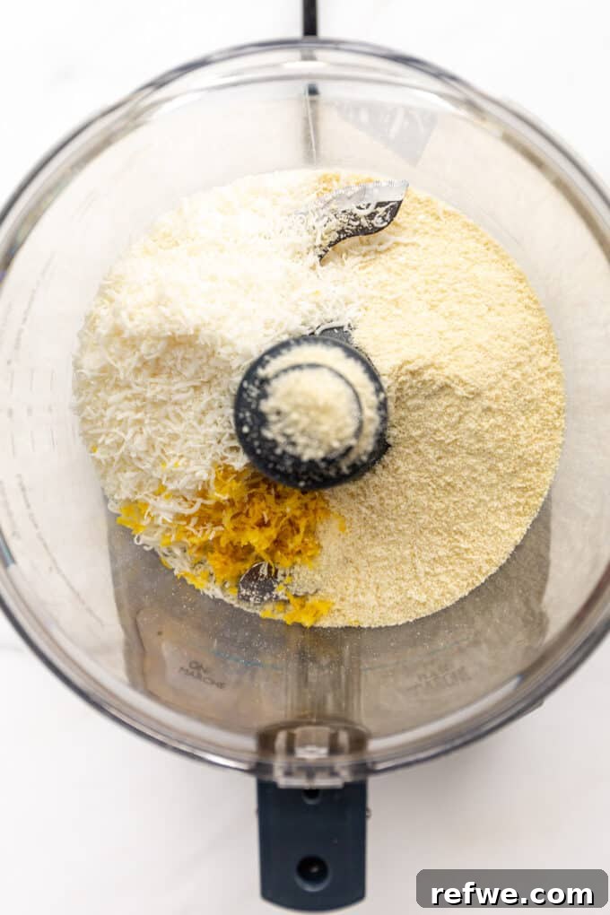 Zesty Lemon Bites 3 Almond flour, shredded coconut, and lemon zest are visible in the basin of a food processor, ready to be pulsed.