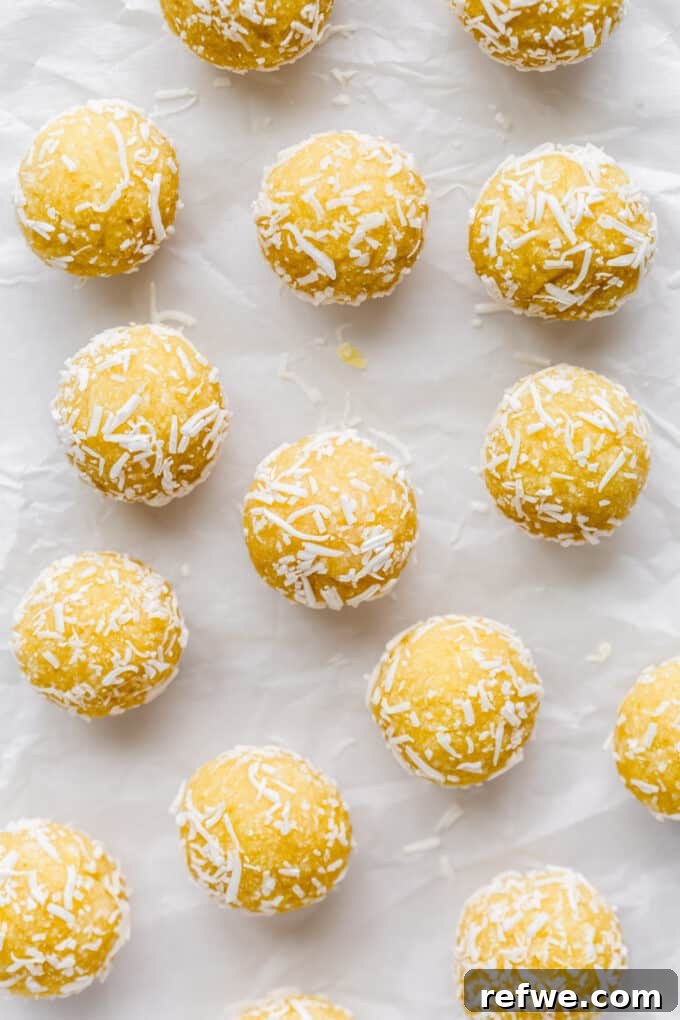 Zesty Lemon Bites 7 A close-up of several lemon bliss balls, perfectly round and coated in shredded coconut, resting on parchment paper.