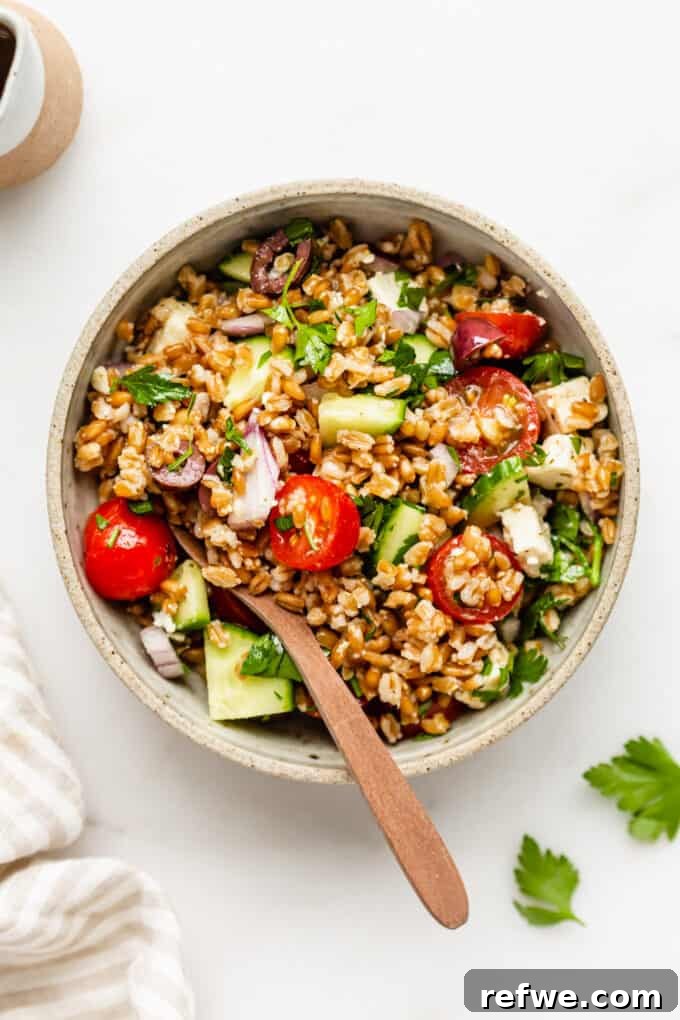Mediterranean Farro and Feta Salad 2 A beautifully presented bowl of Greek Farro Salad, accompanied by a wooden spoon, on a rustic background.