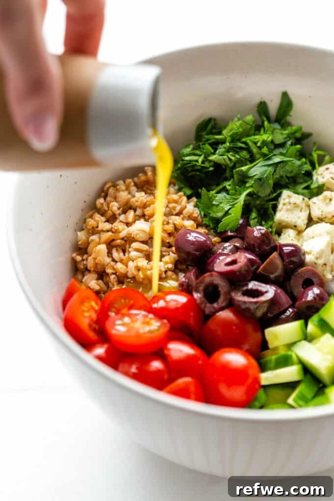 Mediterranean Farro and Feta Salad 5 A stream of zesty Greek salad dressing being poured over a large bowl of fresh farro salad ingredients.
