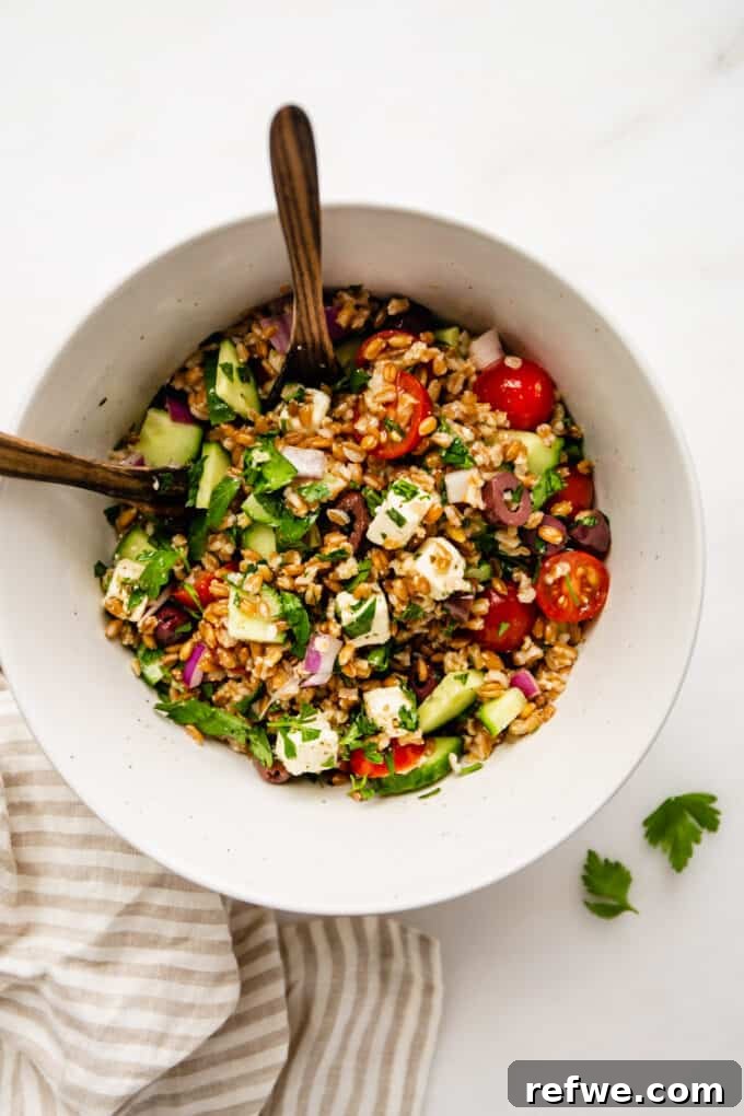 Mediterranean Farro and Feta Salad 6 A vibrant bowl of Greek farro salad, elegantly arranged with serving spoons and a striped napkin on the side, ready to be enjoyed.