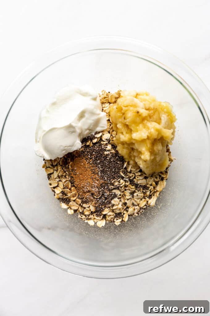 Creamy Banana Overnight Oats 5 Mashed banana, creamy yogurt, a liquid sweetener like maple syrup, and vanilla extract being carefully added to the dry oat and spice mixture in a mixing bowl.