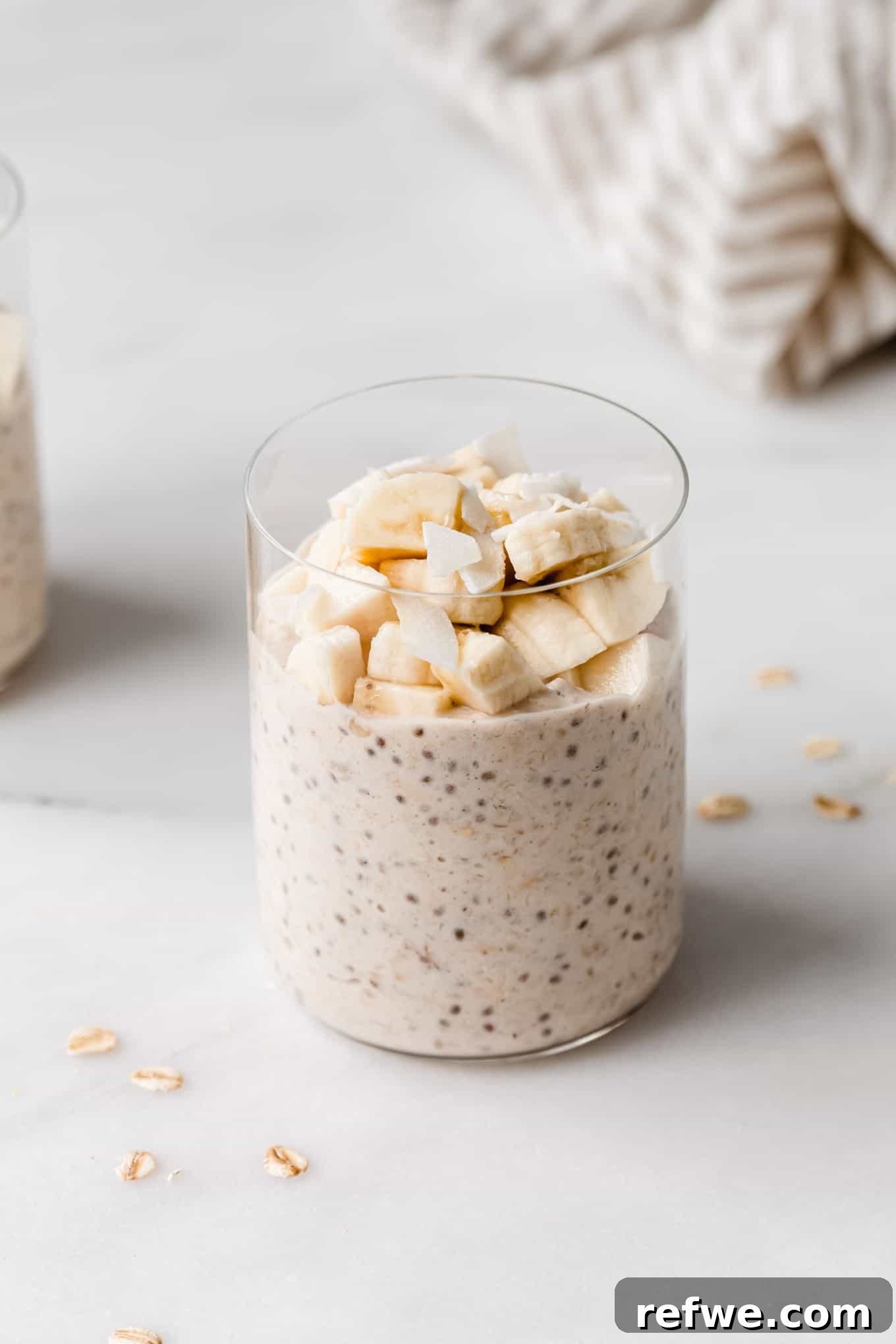 Creamy Banana Overnight Oats 10 A vibrant glass of banana overnight oats, beautifully garnished with fresh banana slices and a delicate sprinkle of toasted coconut flakes, presented as a delightful and healthy breakfast option.