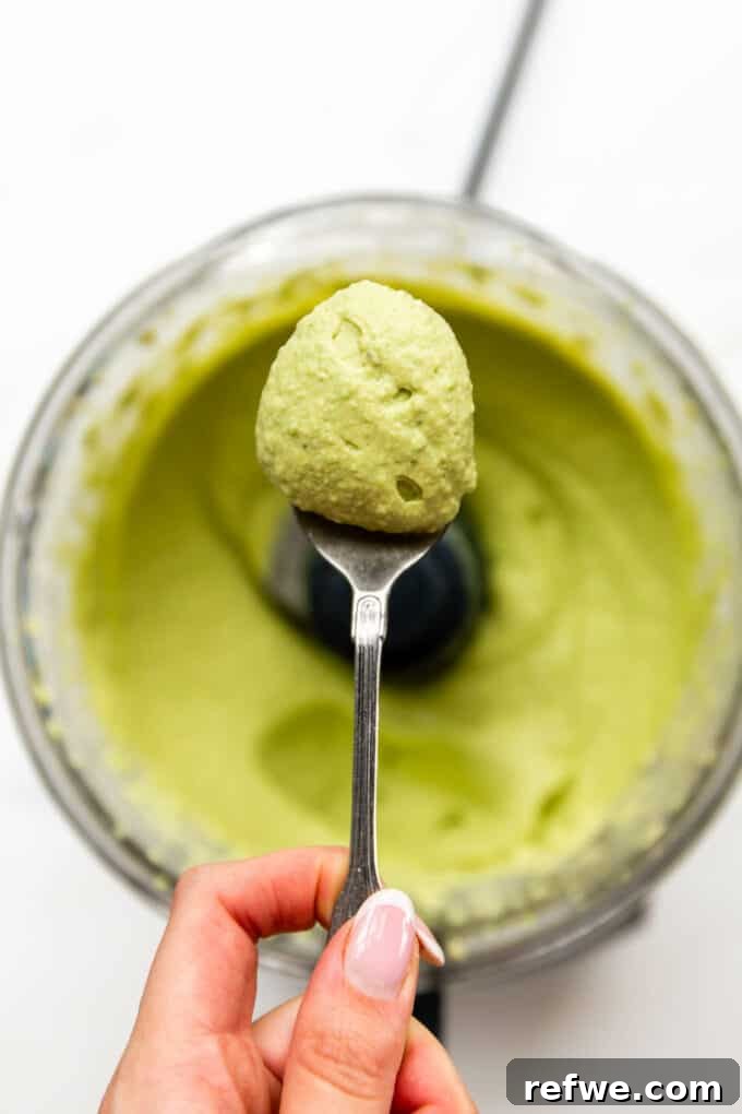 A spoon scooping a generous portion of creamy green pea hummus, highlighting its rich texture.
