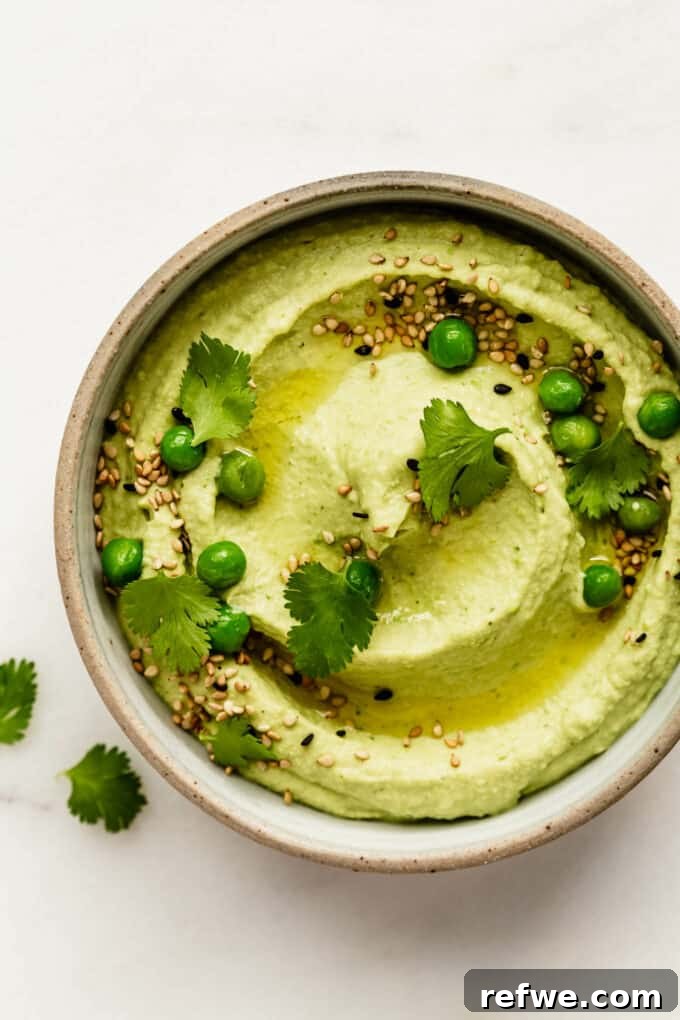 A beautifully presented bowl of green pea hummus, garnished with fresh cilantro, whole green peas, and a drizzle of olive oil, ready to be served.