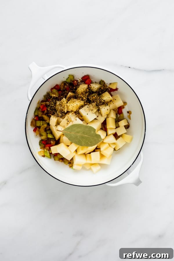 A pot filled with sautéed vegetables, diced potatoes, and dried herbs, ready for the liquid ingredients.
