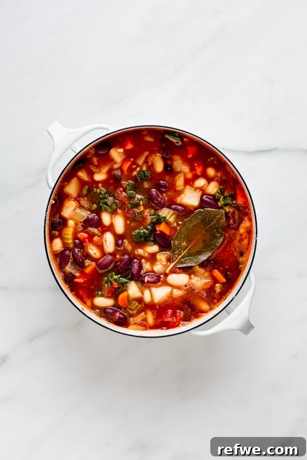 A large pot brimming with rich, colorful vegan minestrone soup, featuring visible vegetables, beans, and pasta.