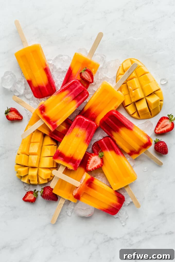 strawberry mango popsicles on a marble board with mangos and strawberries