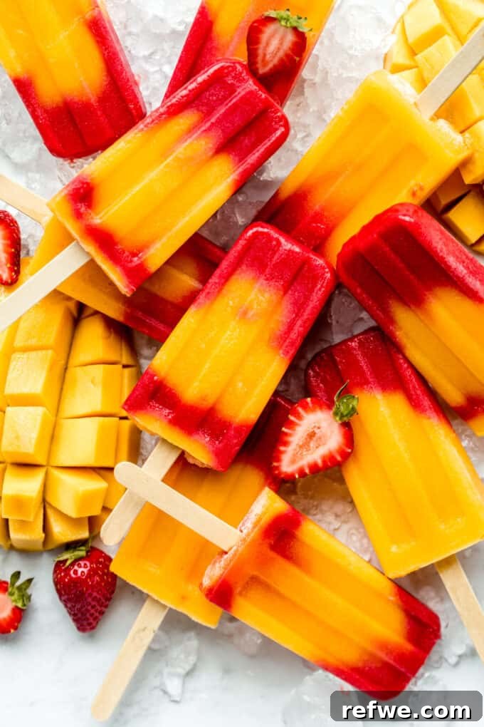 strawberry mango popsicles on ice with sliced strawberries and mango around them