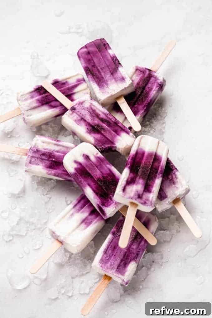 Beat the Heat: 8 Refreshing Homemade Popsicle Ideas 4 Three creamy purple Blueberry Greek Yogurt Popsicles with visible blueberry swirls, standing in a small glass container, emphasizing their rich texture.