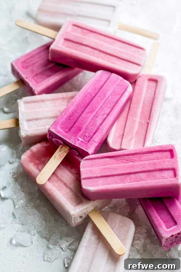 Beat the Heat: 8 Refreshing Homemade Popsicle Ideas 9 Three vibrant pink Raspberry Coconut Creamsicles, layered with distinct fruit and creamy textures, elegantly presented in a glass on a patterned cloth.