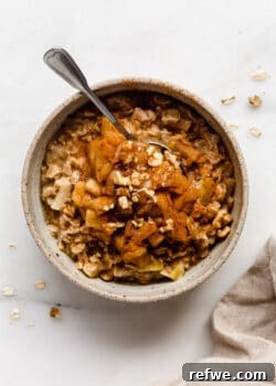 A bowl of apple pie oatmeal, beautifully presented with cooked apple slices and a sprinkle of nuts on top.