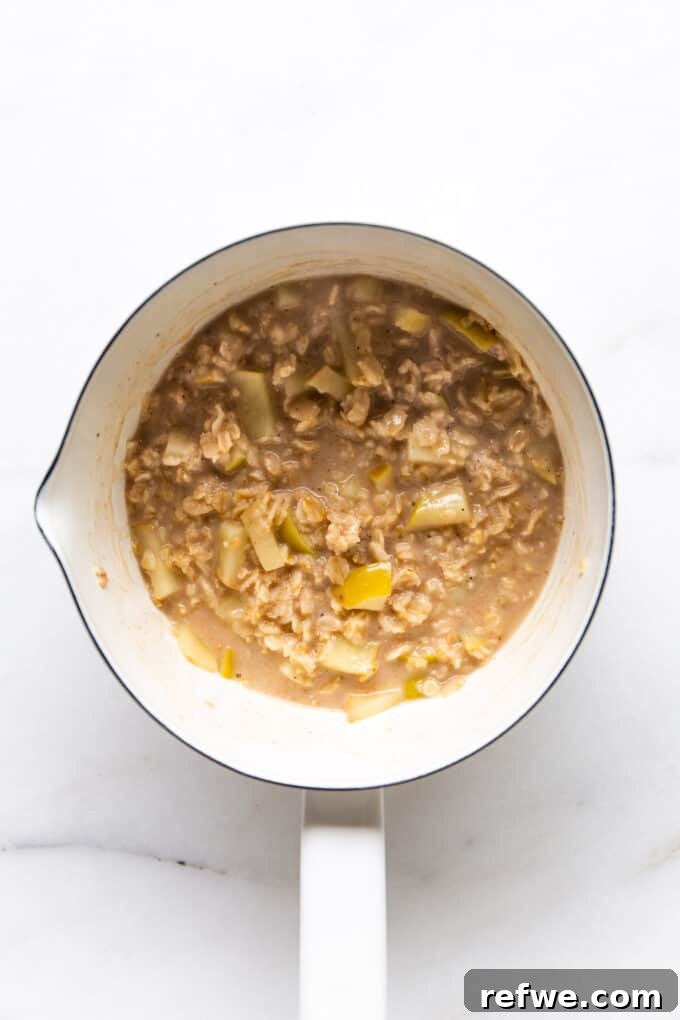 Warm Apple Pie Oats 8 Apple pie oatmeal gently simmering in a white pot on the stove, thickening to a creamy consistency.