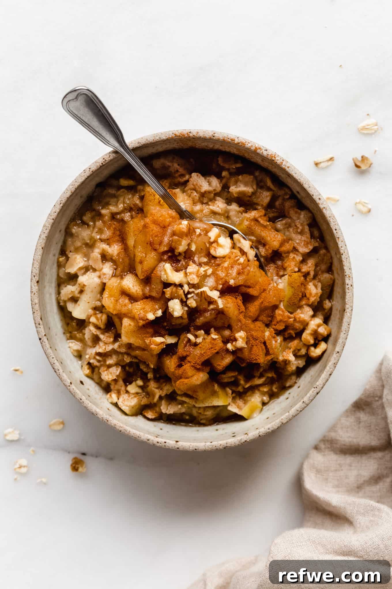 Warm Apple Pie Oats 10 A close-up shot of a bowl of creamy apple pie oatmeal, generously topped with tender cooked apples, a dusting of cinnamon, and crunchy walnuts.