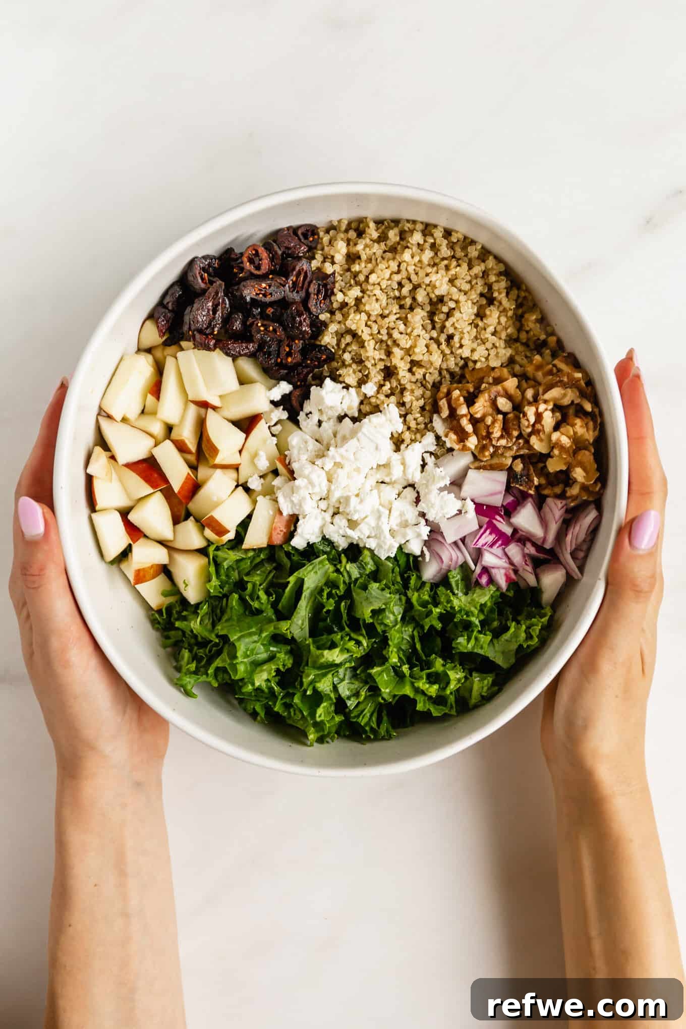 Vibrant Apple Cranberry Quinoa Salad 4 Two hands gently holding a large mixing bowl filled with vibrant ingredients for apple quinoa salad, ready to be tossed.