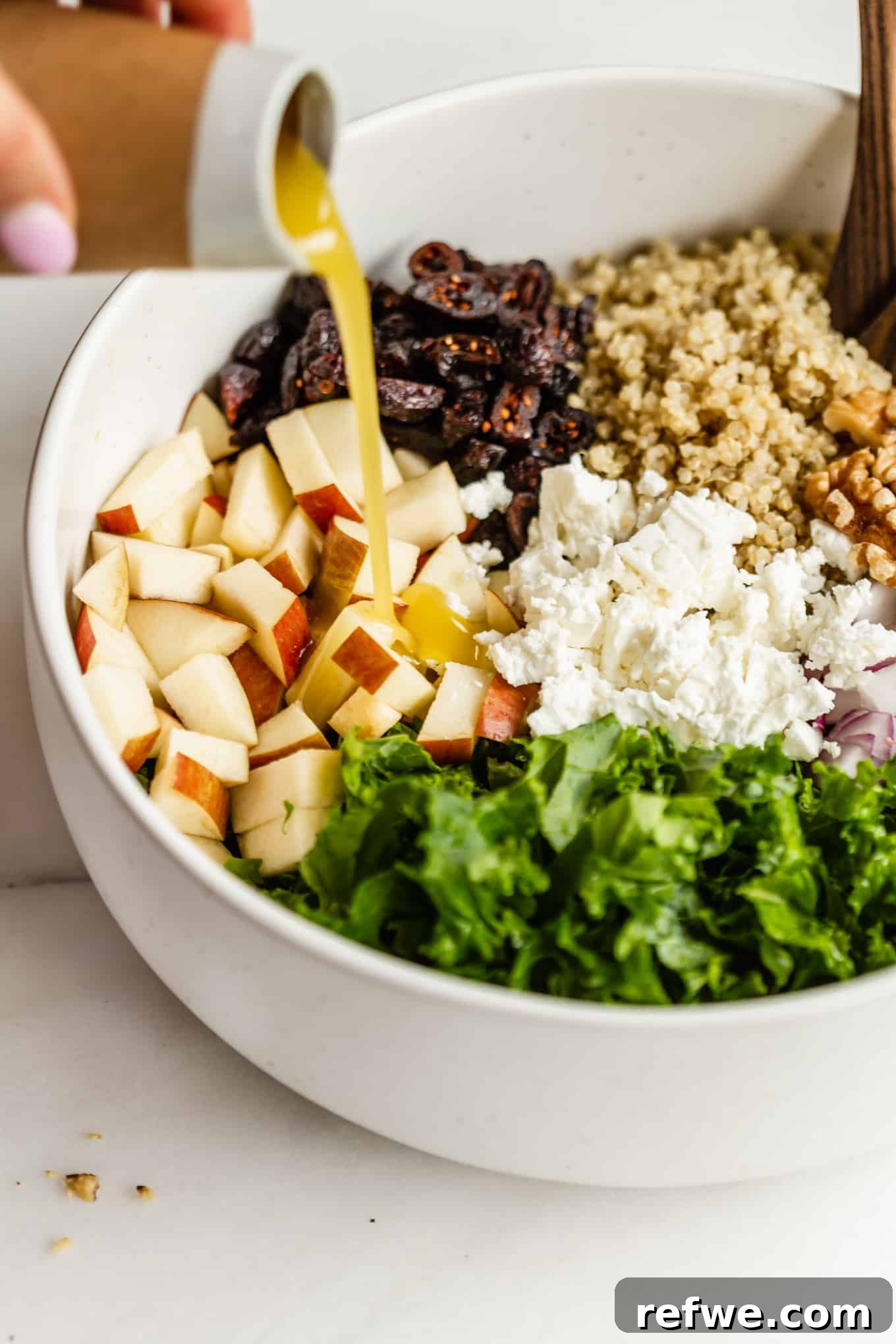 Vibrant Apple Cranberry Quinoa Salad 5 A stream of homemade salad dressing being poured over a colorful bowl of apple quinoa salad ingredients.