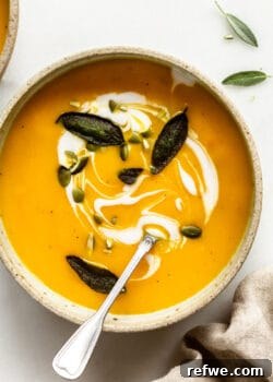 A bowl of creamy roasted acorn squash soup, garnished with crispy fried sage leaves and crunchy pumpkin seeds, ready to be enjoyed on a chilly autumn day.