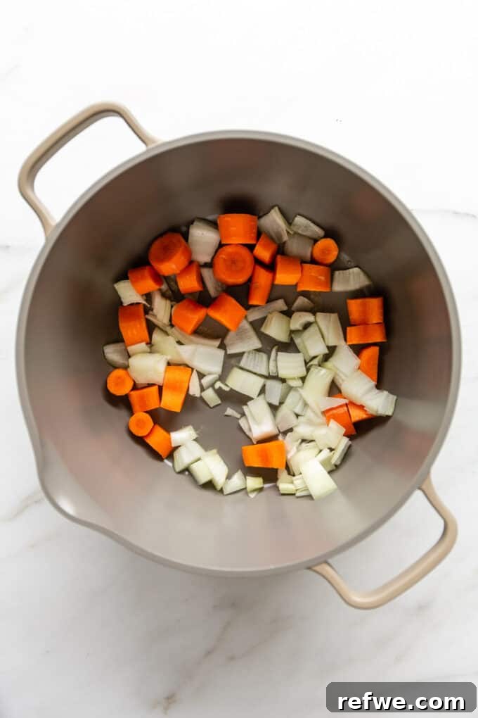 Roasted Autumn Acorn Bliss 6 A large pot on a stovetop, filled with finely chopped onions, minced garlic, and diced carrots, gently sautéing in oil to develop their aromatic flavors.