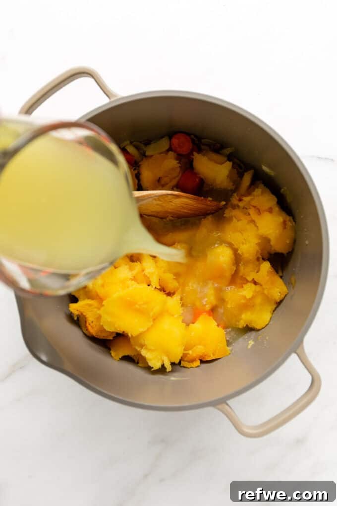 Roasted Autumn Acorn Bliss 8 Vegetable broth being carefully poured into a large pot filled with roasted acorn squash and sautéed aromatics, initiating the simmering process for the soup.