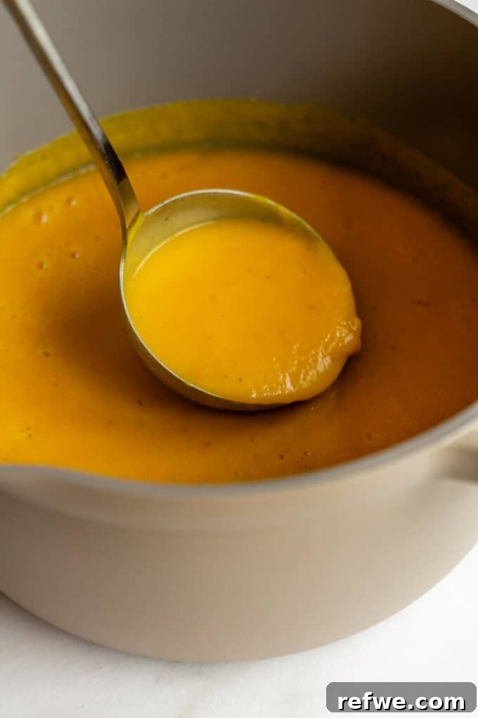 Roasted Autumn Acorn Bliss 10 A ladle expertly spooning out rich, creamy roasted acorn squash soup from a large pot, showcasing its velvety texture.
