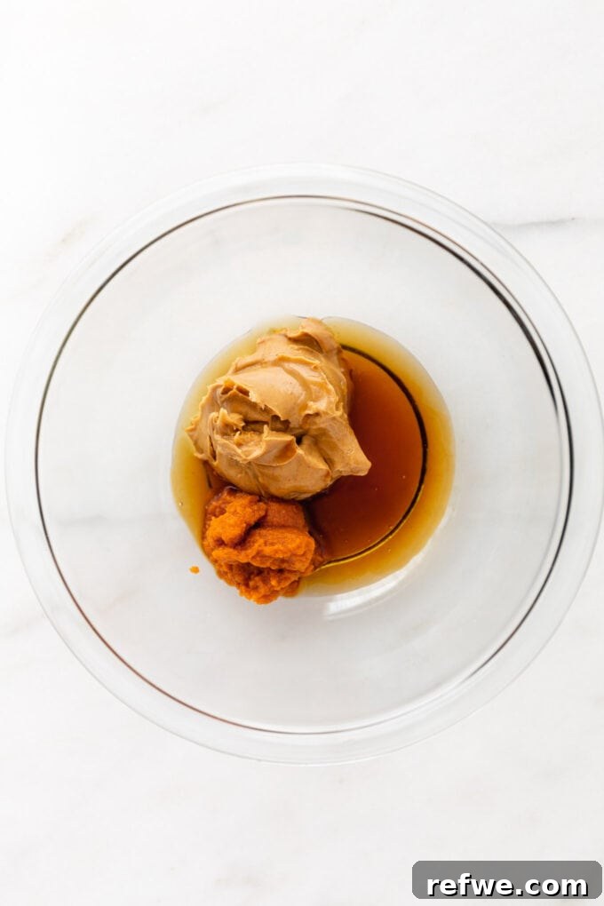 Maple syrup, cashew butter, and pumpkin puree being combined in a mixing bowl.