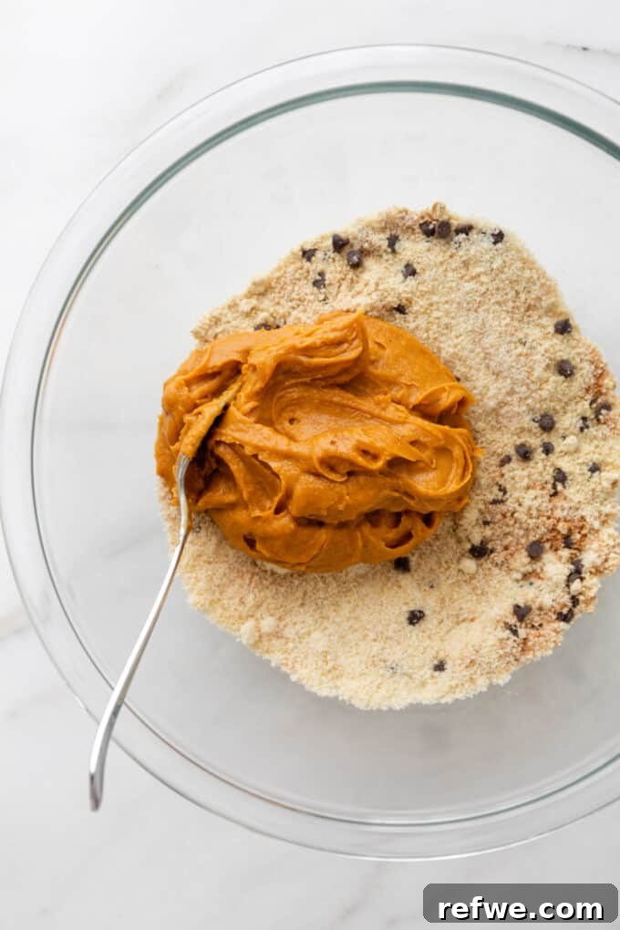 The wet pumpkin puree mixture being poured into the bowl of dry ingredients: almond flour, chocolate chips, and spices.