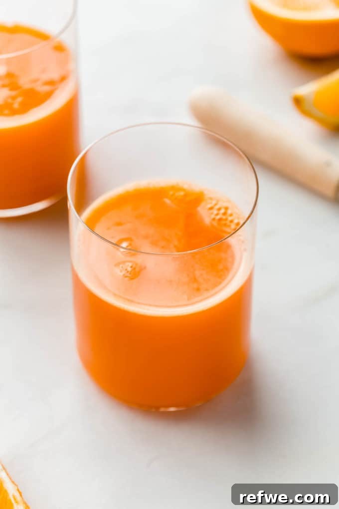 Zingy Ginger Carrot Orange Immunity Nectar 2 A refreshing glass of immune boosting orange and carrot juice, with fresh oranges in the blurred background, suggesting natural ingredients.
